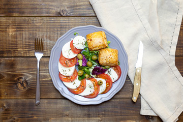 Caprese salad with tomatoes, fresh herbs, mozzarella, olive oil, basil, olives on dark rustic wood texture, top view