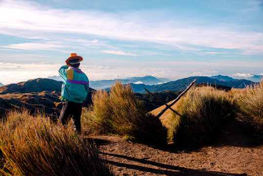 An adult man in light blue jacket and orange hat standing at the peak of Mt. Pulag National Park enjoying the breathtaking view of the sea of clouds