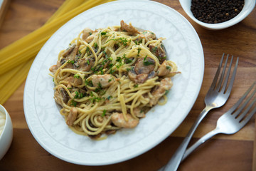 Mushrooms over spaghetti . Raw spaghetti pasta inside a bowl . Black pepper, Mayonnaise inside a bowl. Forks . Uncooked spaghetti . Delicious spaghetti wooden tray .