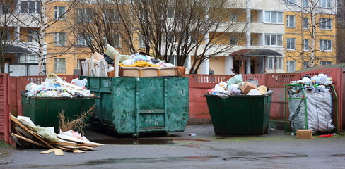 Fototapeta na wymiar Overflowing with household waste bins in the yard of a residential building