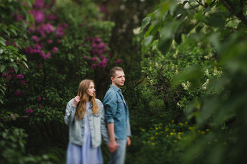 Romantic and happy caucasian couple in casual clothes hugging on the background of beautiful blooming lilac. Love, relationships, romance, happiness concept. Man and woman walking outdoors together.