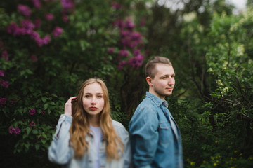 Obraz premium Romantic and happy caucasian couple in casual clothes hugging on the background of beautiful blooming lilac. Love, relationships, romance, happiness concept. Man and woman walking outdoors together.