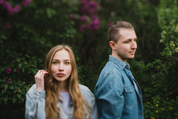 Fototapeta premium Romantic and happy caucasian couple in casual clothes hugging on the background of beautiful blooming lilac. Love, relationships, romance, happiness concept. Man and woman walking outdoors together.