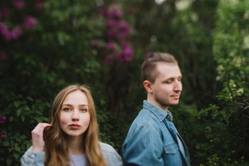 Fototapeta premium Romantic and happy caucasian couple in casual clothes hugging on the background of beautiful blooming lilac. Love, relationships, romance, happiness concept. Man and woman walking outdoors together.