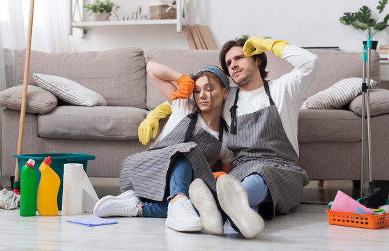 Portrait Of Exhausted Couple Resting On Floor After Spring-Cleaning Home