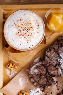 Cup of coffee with aromatic foam and cinnamon, cookies and jam on a rustic background. Top view. Photo for advertising or banner.