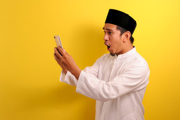 Happy Shock Young Asian Muslim man wearing muslim clothes holding mobile phone look at phone screen