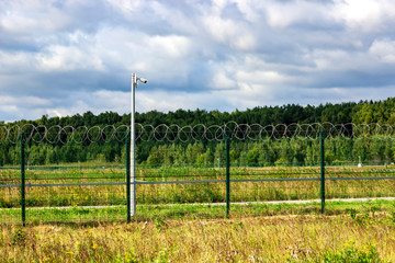 Fototapeta premium Fence, barbed wire and video camera. Obstruction and surveillance observation.