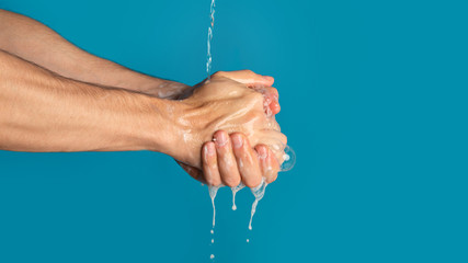 Unrecognizable millennial guy washing his hands with soap on blue background, copy space. Panorama