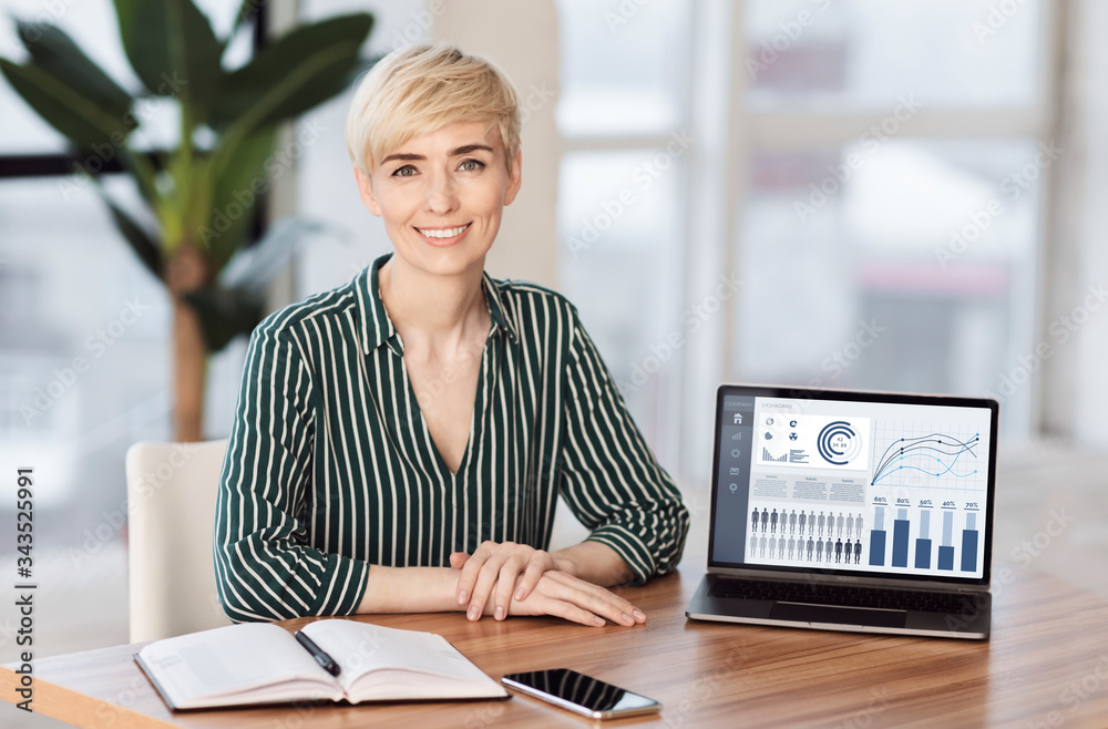 Wall mural smiling female manager sitting at desk with laptop