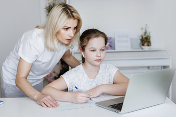 Girl with mom at the table with laptop.