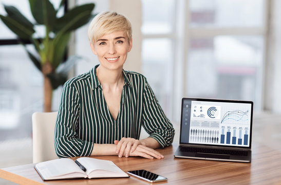 Smiling female manager sitting at desk with laptop
