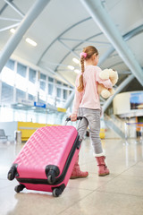 Fototapeta na wymiar Little girl with suitcase and stuffed animal is traveling alone