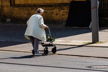 An old Lady with a walker crosses a street, old woman with rollator