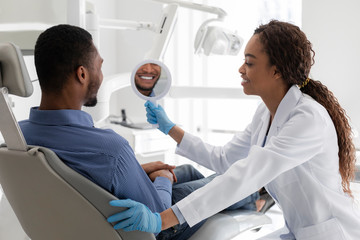 Obraz premium Dentist and patient checking smile in mirror after whitening procedure