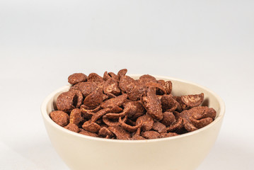 Chocolate corn flakes falling to the white bowl isolated on white. Motion.