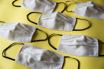 Handmade face protective masks on yellow flat lay background. Pattern of reusable linen face masks against coronavirus, covid-19, flu or pollution.