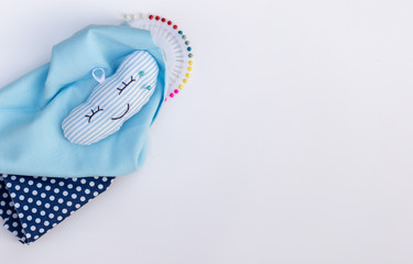 Multi-colored set pins for sewing in a smiling pillow for pins. Needlework concept.white background. Pieces of blue fabric