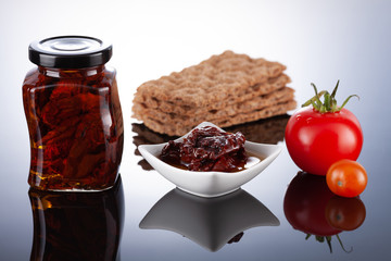 Dried tomatoes in olive oil preserved in a glass jar on a light background.