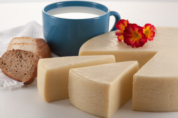Yellow cheese made from cow's milk and a blue glass of milk and bread.