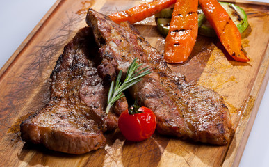Black Angus steak grilled on a wooden board and garnished with vegetables