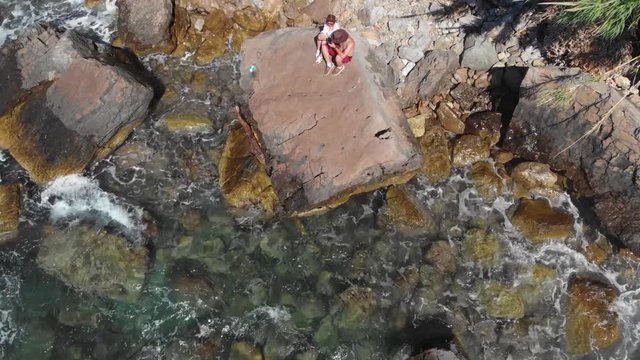 View of rocky paradise beach, couple of tourists is sitting and look at distace. coastline of the village of Nerano. Wild beach of Italy. Turquoise, blue surface of the water. Vacation and travel