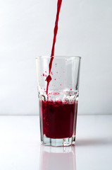 Splashing liquid red pomegranate and grape juice pouring into a glass