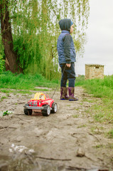 a child in a blue yolk and rubber boots carries a typewriter by a rope through the mud. A child walks outside after a summer rain. A concept of a carefree childhood.