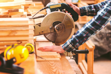 Closeup skilled cabinet maker cutting wood board with electric circular saw at woodworking sawmill. Professional cabinet maker use circular saw at sawmill factory. Wooden furniture production. Joinery - obrazy, fototapety, plakaty