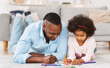 Quiet family times. Pretty African American girl drawing on floor with her granddad