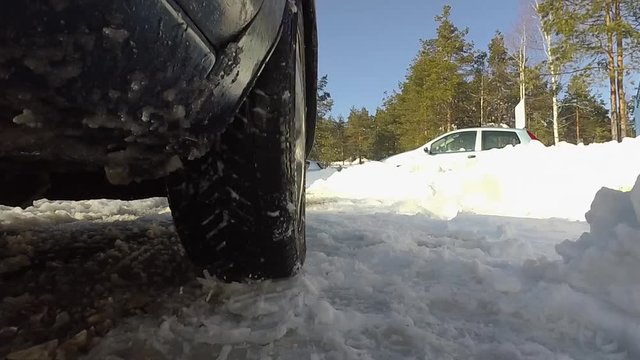 Car wheel spins, drives through the area with snow. Shot from below, throws snow at the camera.