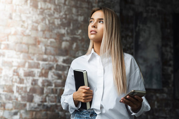 Fototapeta premium Beautiful woman standing in brick wall background. Freelance jobs for young specialists. Student with copybook