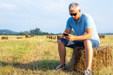 Naklejka na ściany i meble Adult man with a phone sits on a haystack.