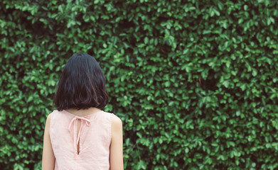 A woman with short hair and pink dressstanding on the background of the Green trees surface. a green natural background. feeling Alone and scared.vintage. Copy space.