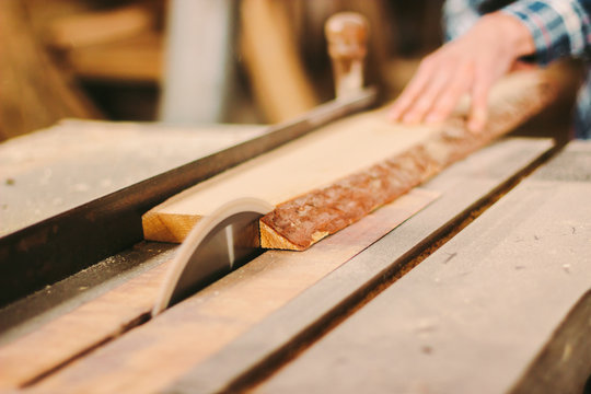 Closeup of wood cutting table with electric circular saw. Man skilled cabinet maker using circular saw at woodworking workshop. Professional carpenter cutting wooden board at sawmill. Sawing machine