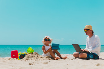 father with laptop and cute daughter with touch pad on beach