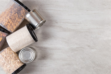 Food supplies, jars of oatmeal and canned rice, on a stone countertop, a view from above.