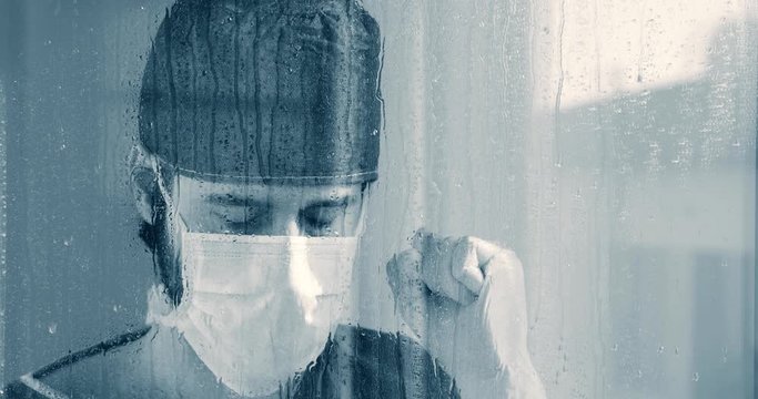 Triste medico affacciato dalla finestra in bianco e nero durante la pioggia.