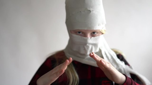 funny video - quarantined due to an epidemic of coronavirus. girl in a mask from toilet paper posing on a gray background.