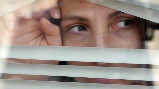 Close-up of a woman's eye looking out into the gap from the blinds. Looking fearfully from the outside, because it is afraid of germs. The concept of quarantine, self-isolation, home isolation.