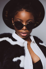 Portrait of an african woman with sunglasses and a black hat in the studio on a white background .