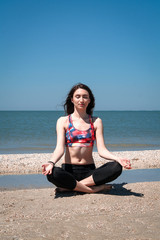 Fototapeta na wymiar Young european woman practicing yoga in lotus position on the beach. Healthy active lifestyle concept. Quarantine is finish