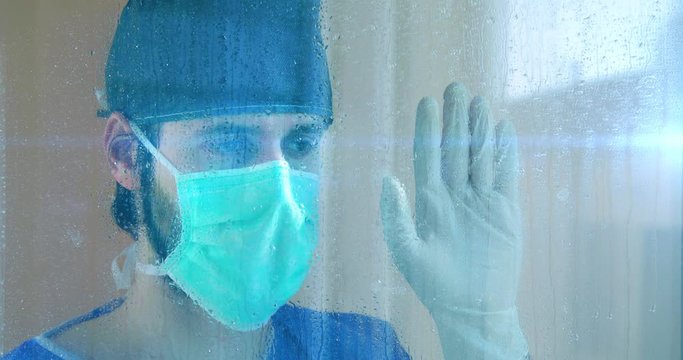 Medico affacciato alla finestra del balcone dell'ospedale durante la pioggia.