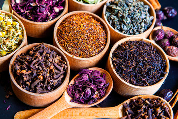 Various dried tea leaves in wooden bowl. Dried herbs tea leaves close up. Different dry herbs and flowers for making healthy tea background.