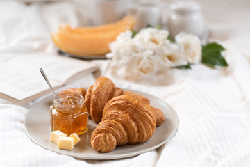 Breakfast in bed with croissants, butter, jam, roses and melon