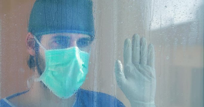 Medico affacciato alla finestra del balcone dell'ospedale durante la pioggia.