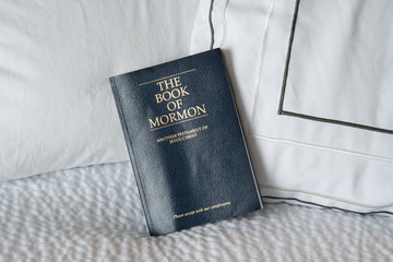 Book of Mormon displayed on bed with white crisp bedding, close up