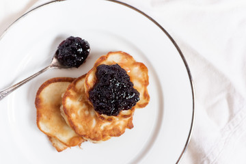 Russian traditional pancakes oladi with blueberry jam on a white plate. Top view.