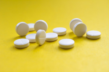 White medical pills on yellow background close-up