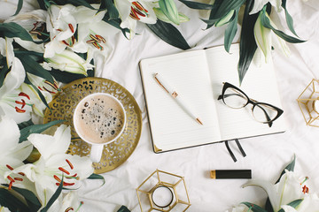 Female pink opened notebook lies on white blanket with coffe cup and flowers. Flat lay, overhead view